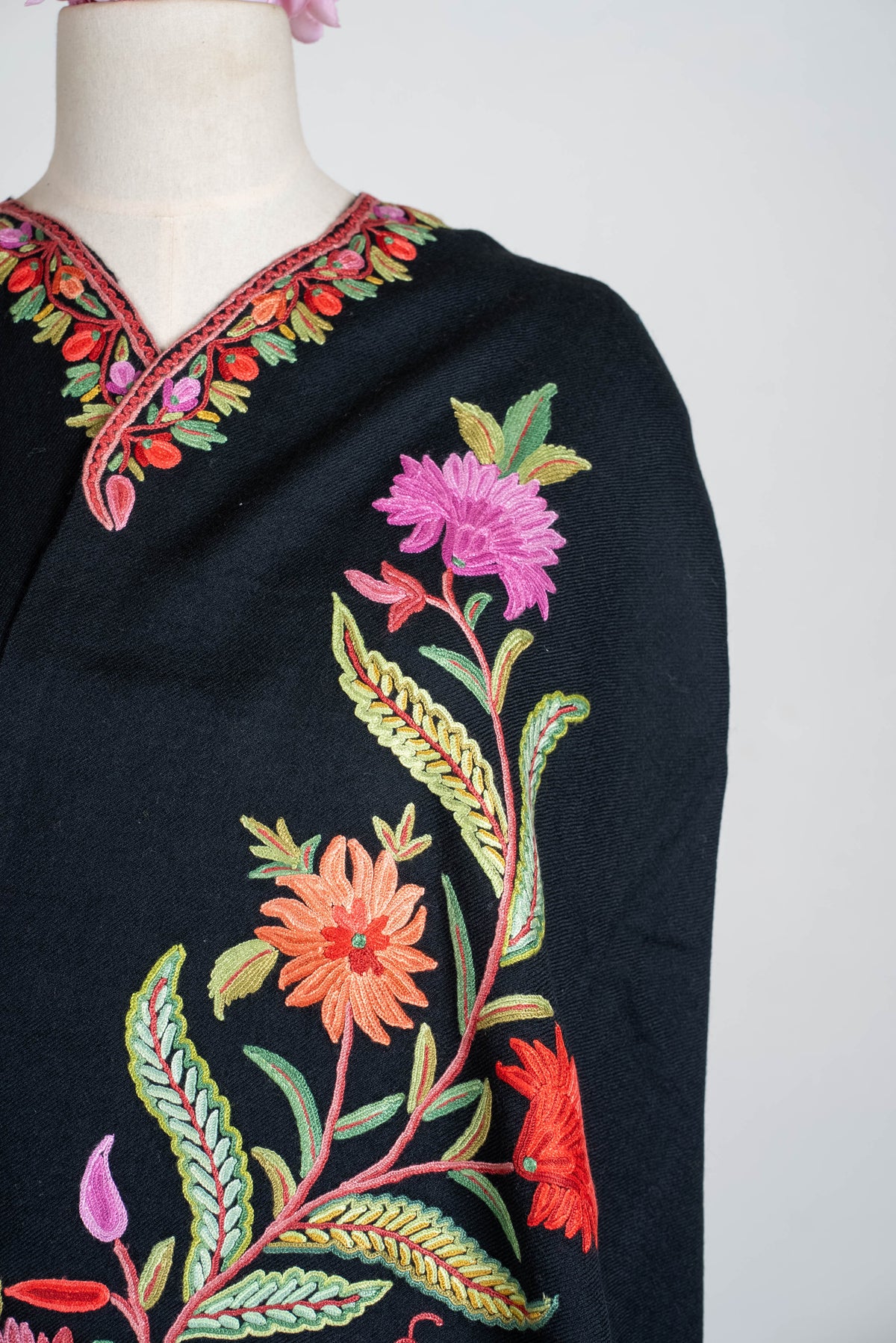 Close-up of the black shawl cape’s front embroidery, with pink and orange flowers on branching stems with green leaves