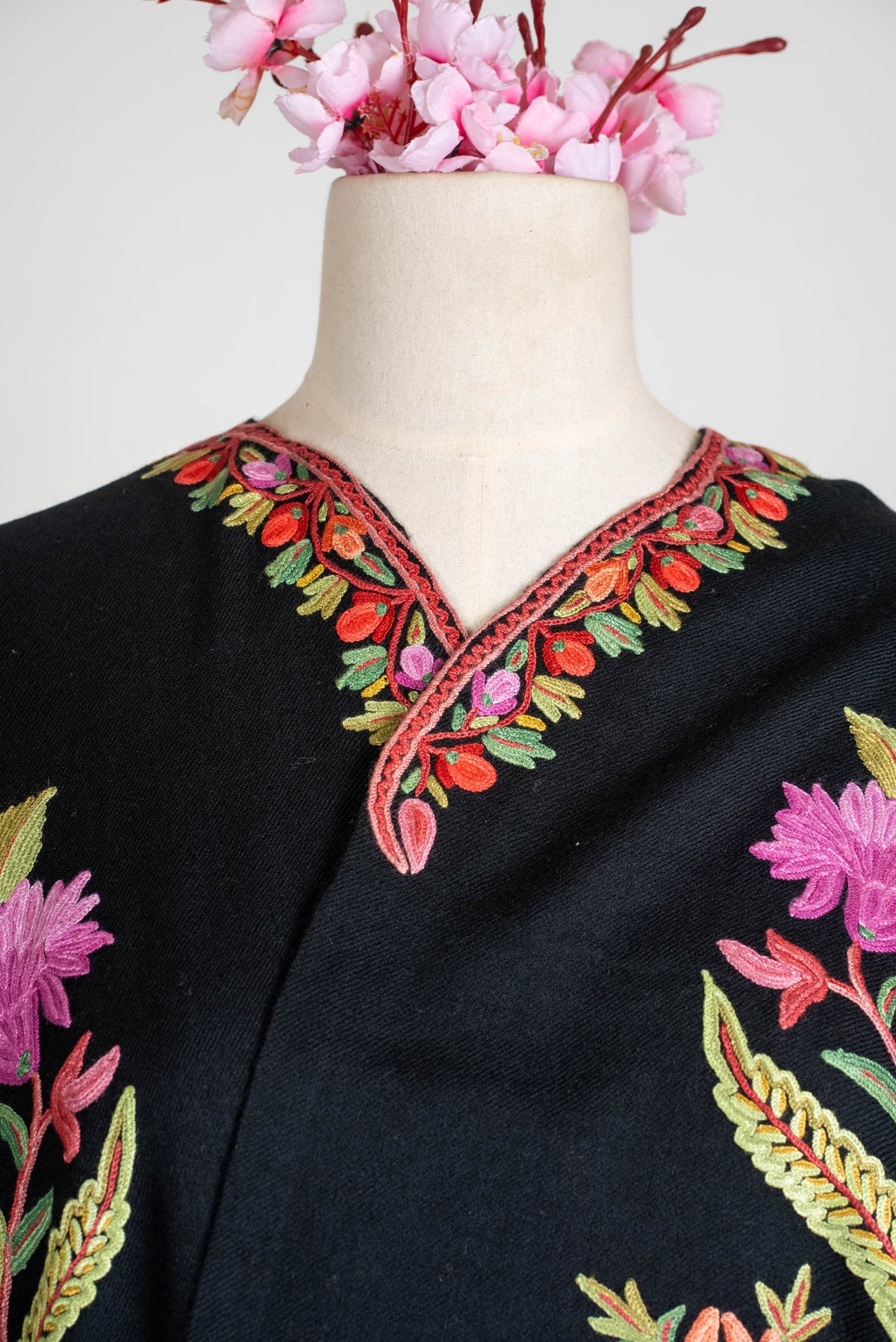 Neckline detail of the black shawl cape, with small red, pink and green embroidered leaves around the curved opening