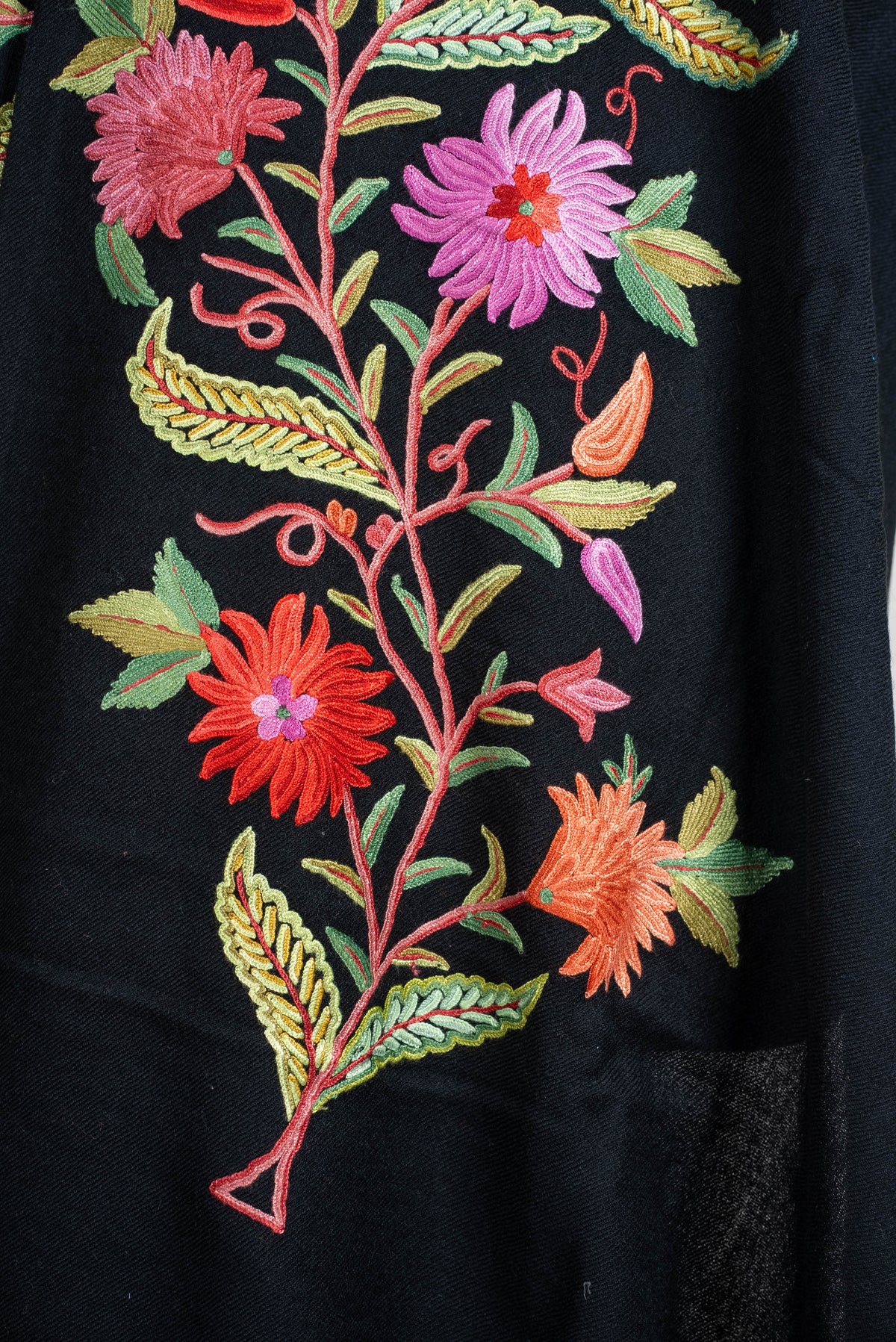 Close-up of pink, coral and orange embroidered flowers with green leaves on the black shawl cape