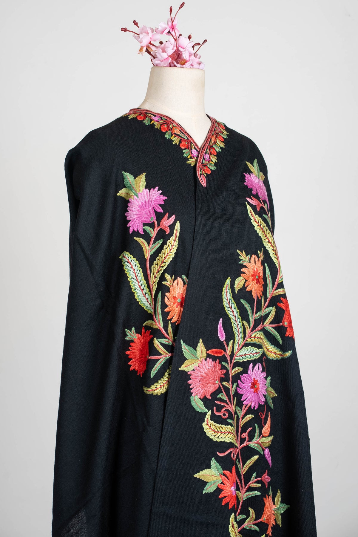 Angled upper-body view of the black shawl cape, with colourful botanical embroidery and a decorated neckline