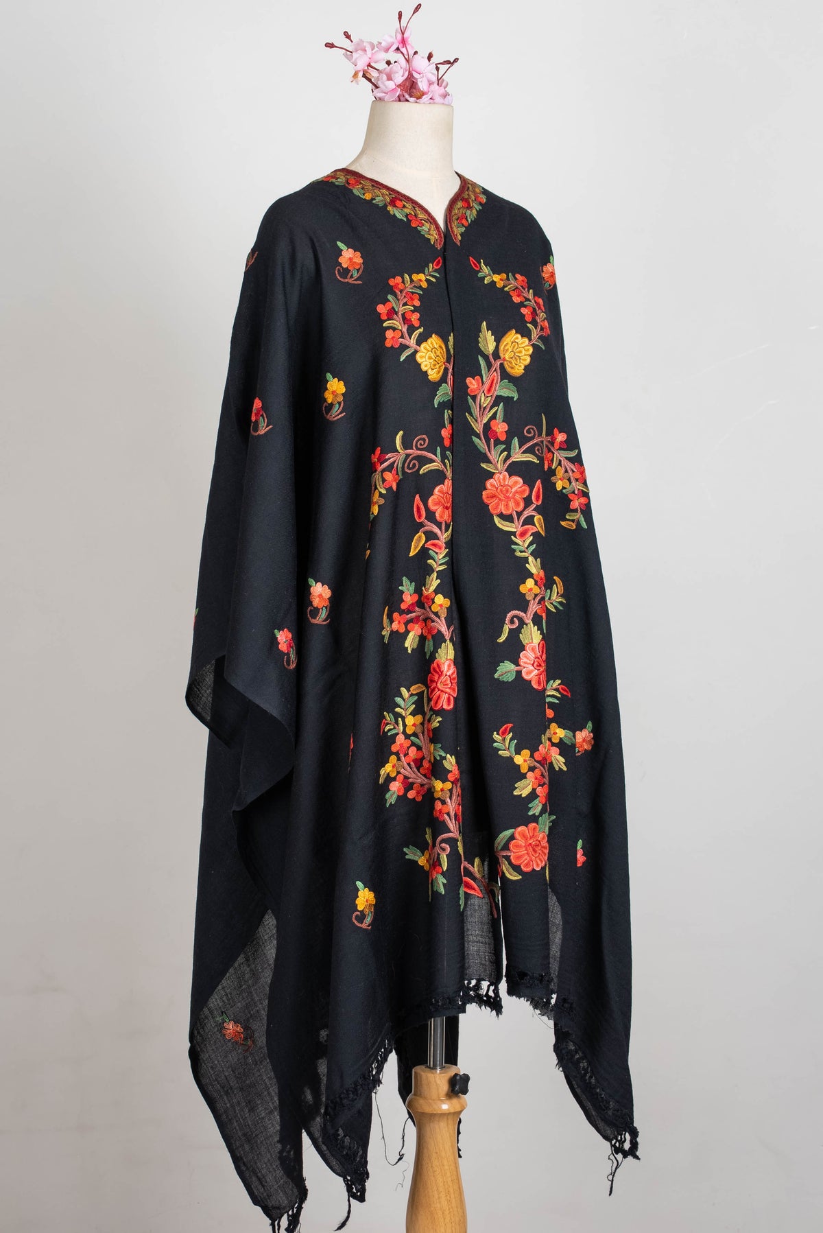Angled full view of the black shawl cape on a mannequin, with coral and yellow floral vines, scattered sprigs and fringed ends