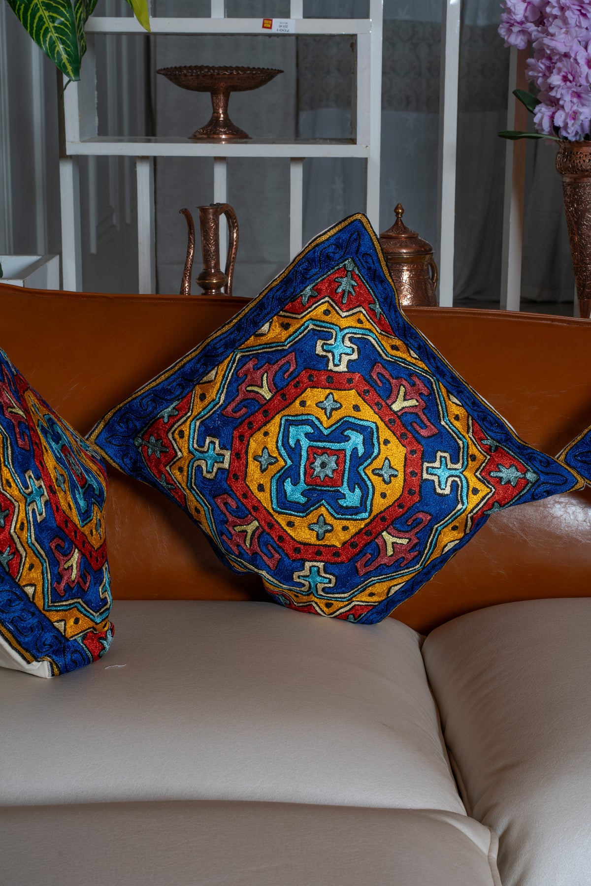 Sapphire blue embroidered cushion with a red and gold medallion resting against a tan sofa back