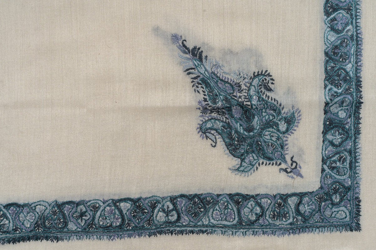 Flat corner detail of an ivory rumal with a teal floral border and a separate ornate paisley motif