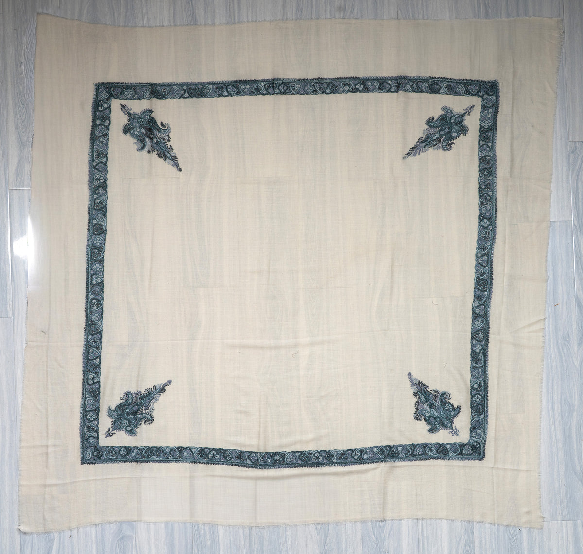 Square ivory Merino wool rumal laid flat, with a dark teal border and four embroidered paisley corner motifs