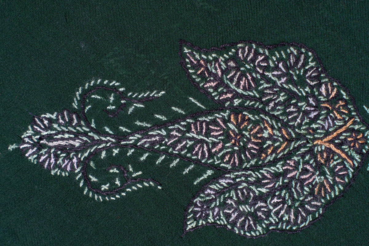 Close-up of a pale embroidered paisley motif with leafy stems and ochre accents on dark green fabric