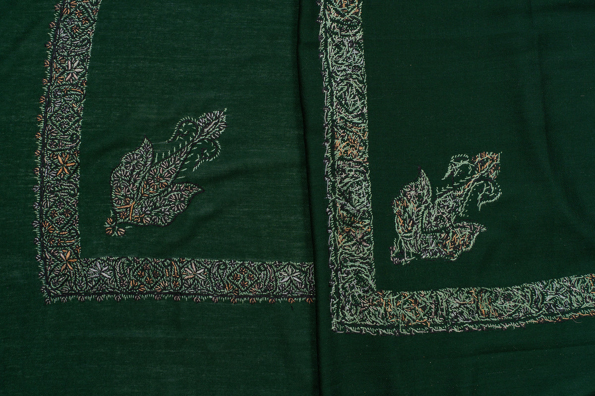 Folded dark green rumal showing the front and reverse of its pale embroidered borders and paisley corner motifs