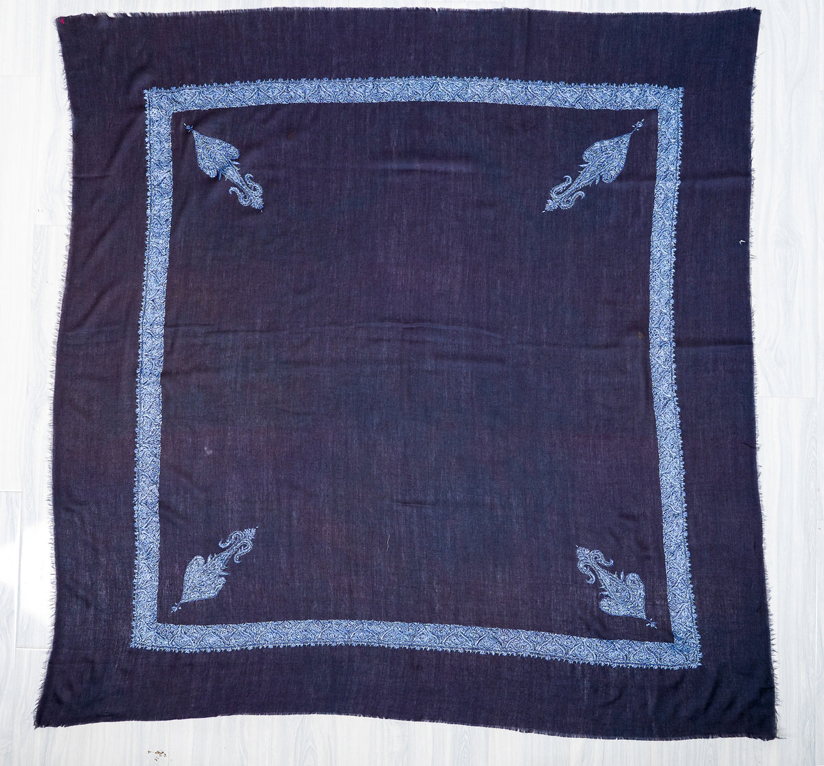 Square dark navy Merino wool rumal spread flat, with a plain centre, icy blue border and four corner motifs