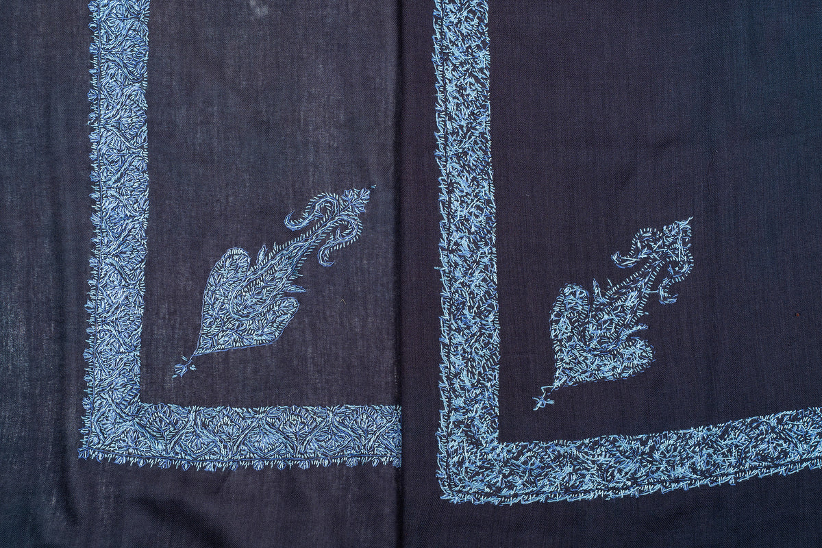 Overlapping dark navy rumal corners showing icy blue embroidered motifs, floral borders and reverse stitching