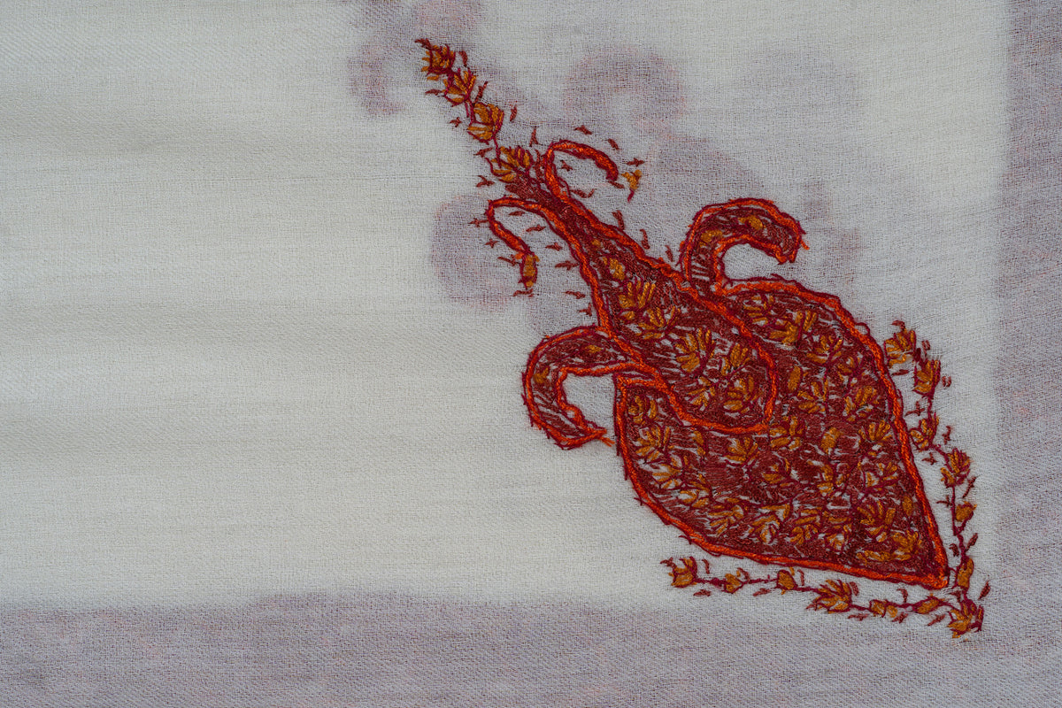 Close-up of a red-orange Sozni motif with curled tips and fine floral stitching on ivory fabric