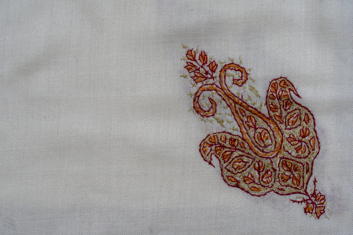 Close-up of a rust and gold Sozni motif with curled tips and fine leaves on ivory fabric