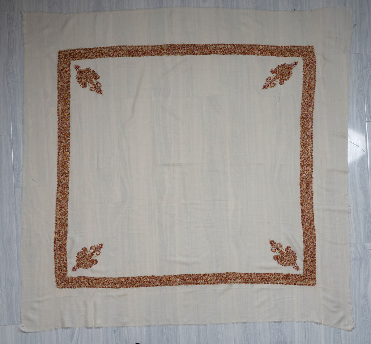 Square ivory Merino wool rumal laid flat with rust and gold Sozni borders, four corner motifs and a plain centre