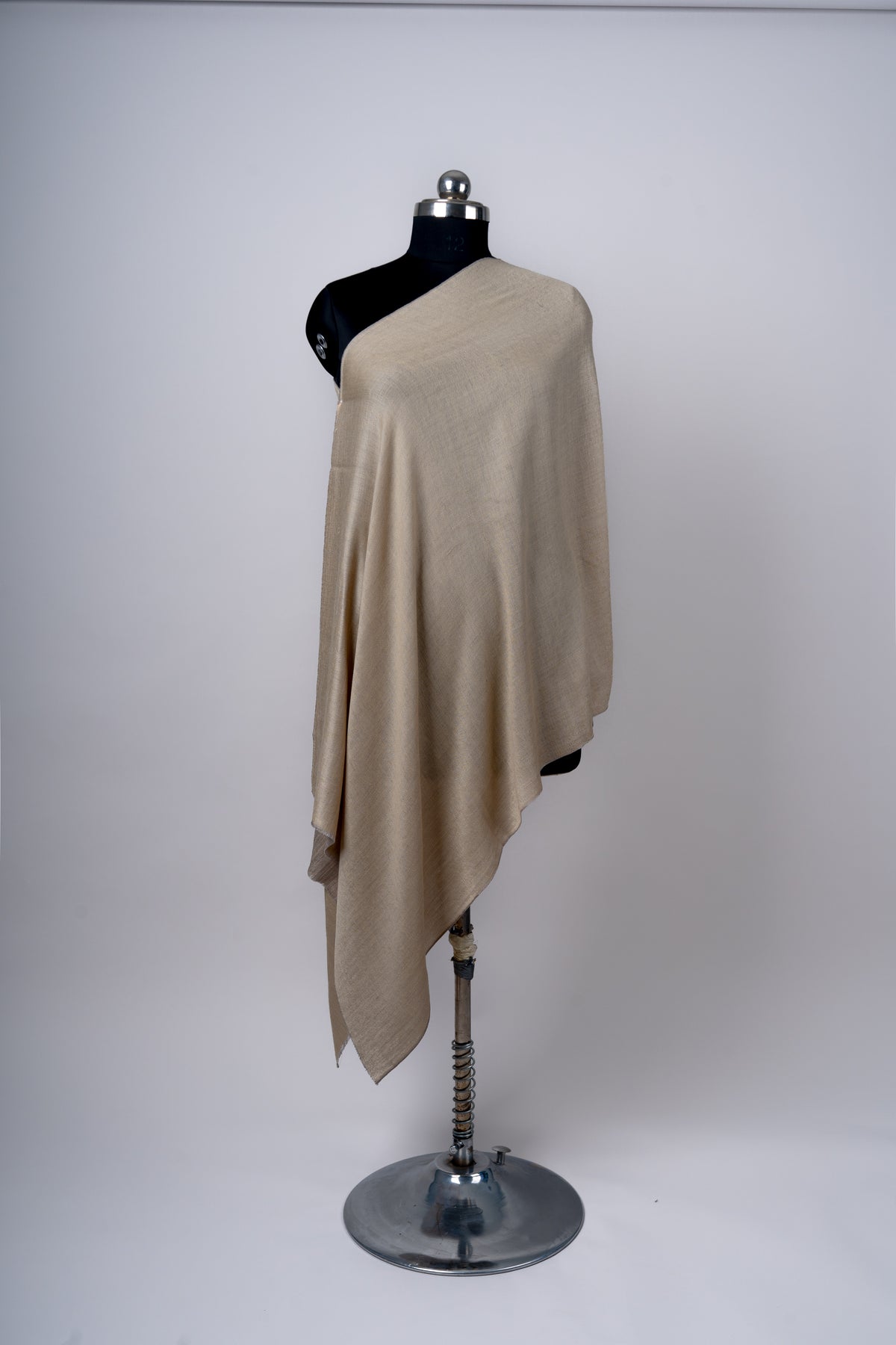 Full-length view of a beige reversible stole draped over a black mannequin, with a long pointed hanging corner