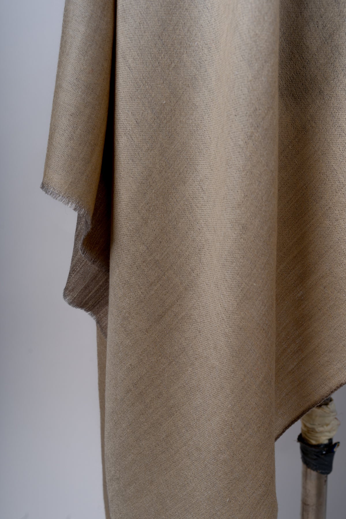 Detail of the beige stole’s hanging folds and short fringe, with a darker sand-coloured reverse visible at the edge