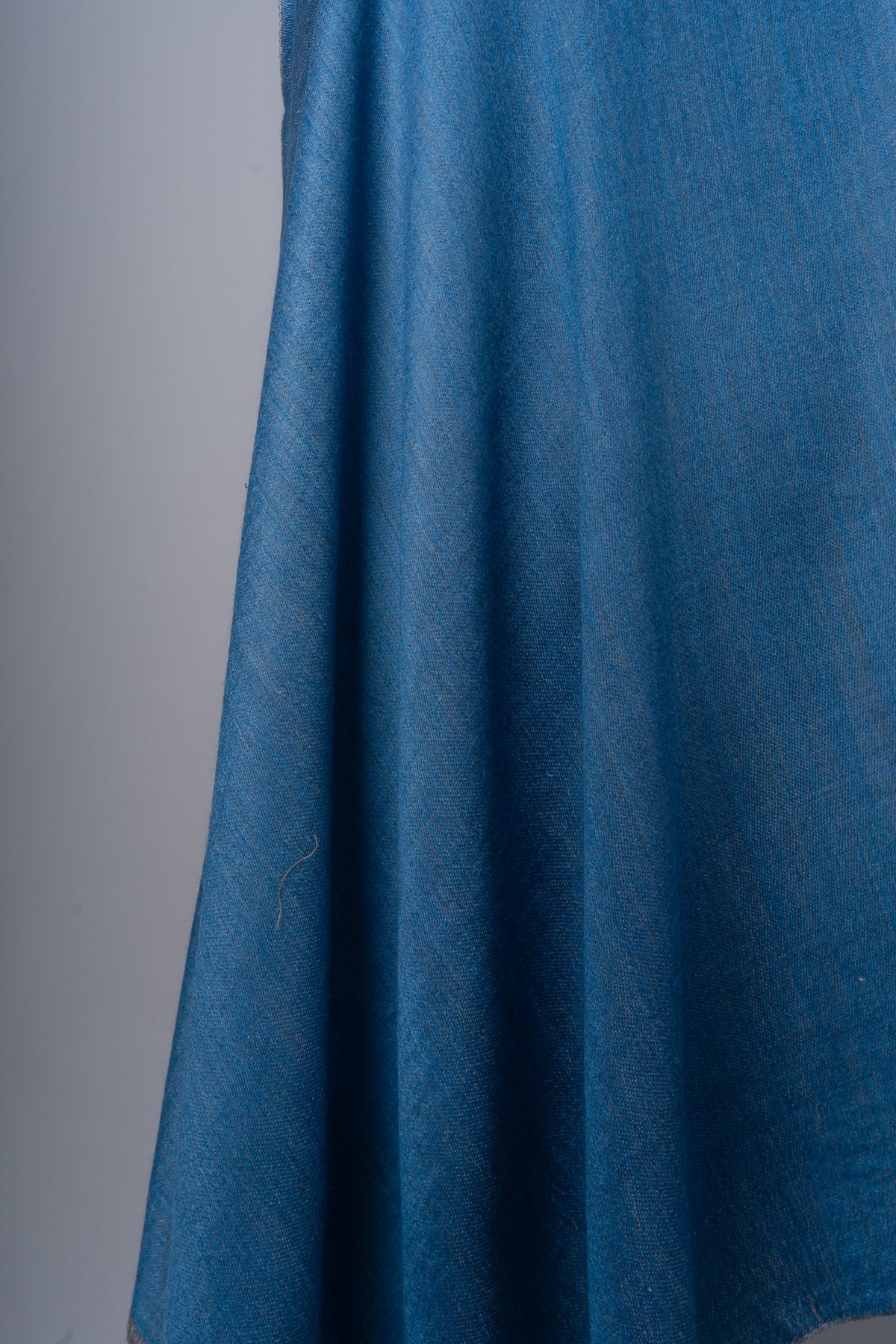 Close-up of the blue stole’s hanging folds, showing its plain surface and fine woven texture.