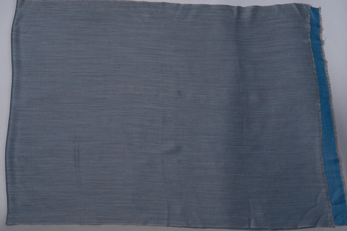 Steel-grey side of the reversible merino wool stole laid flat, with a narrow blue edge visible at one side.