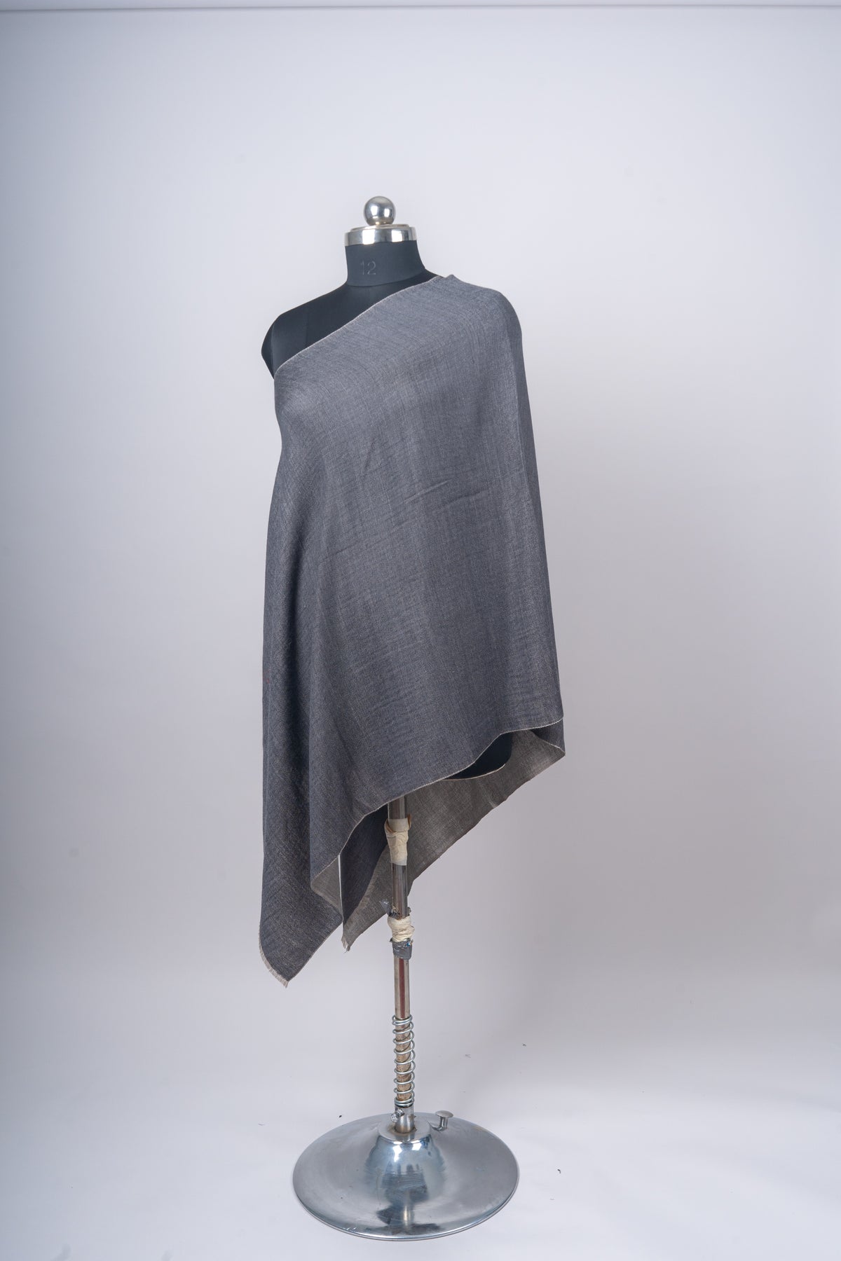 Full mannequin view of the charcoal stole with an asymmetric drape and a lighter reverse edge beneath the front.