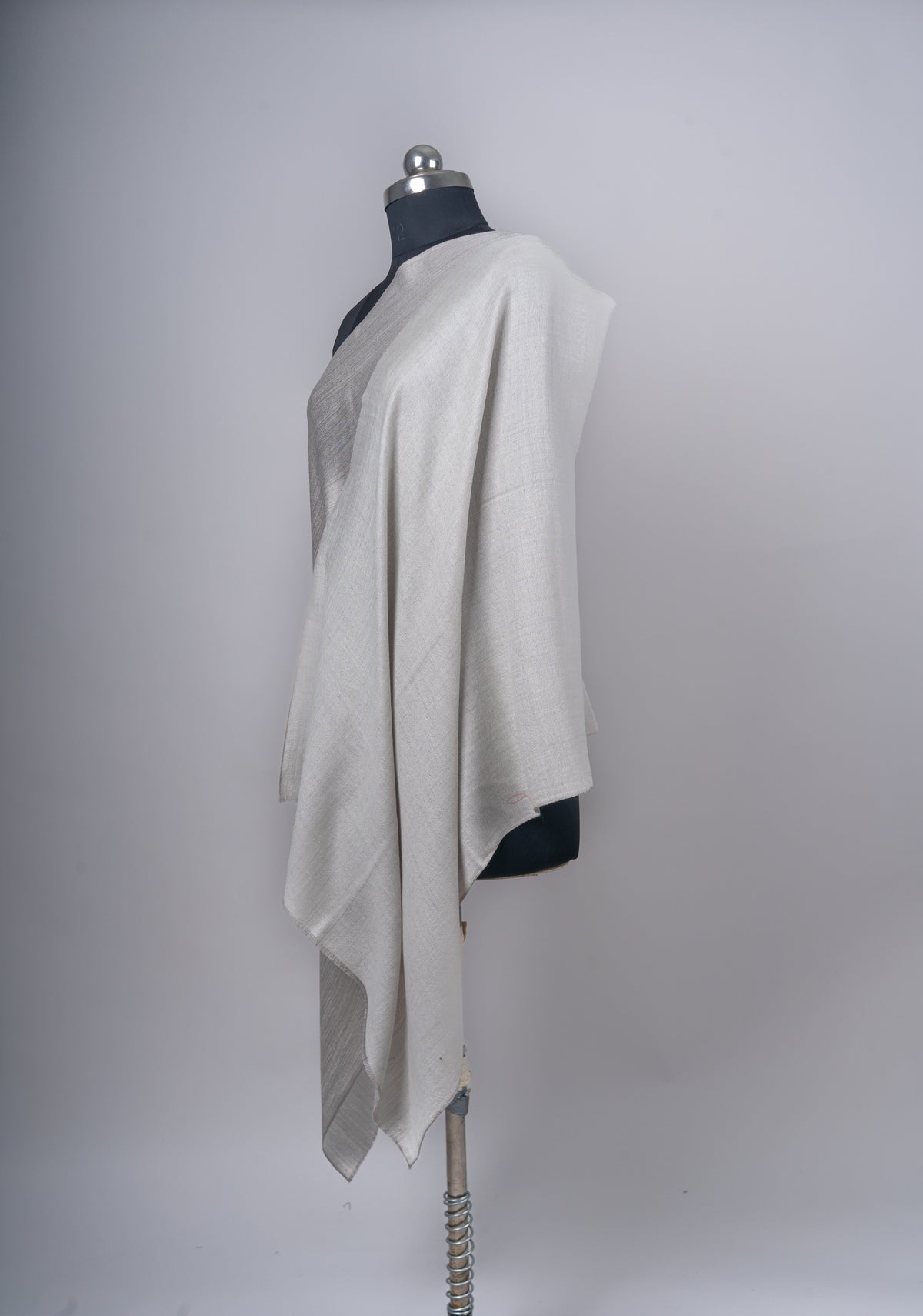 Side view of the reversible ivory and taupe Merino wool stole hanging in long folds from a mannequin’s shoulder