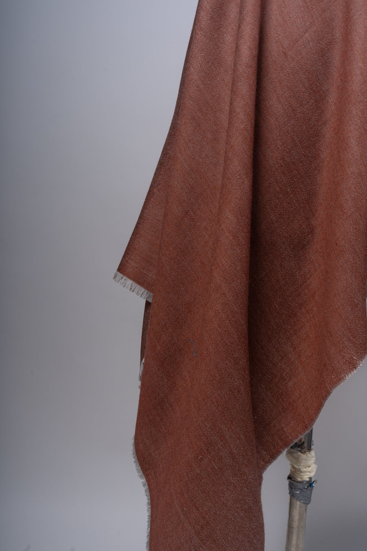 Detail of cinnamon fabric hanging in soft folds, with a sand-grey edge and short fringe
