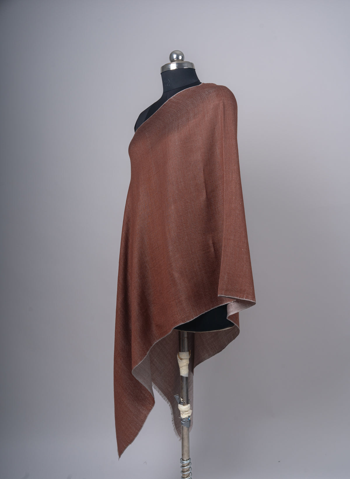 Angled view of the cinnamon stole on a black mannequin, showing its sand-grey reverse along the lower fold
