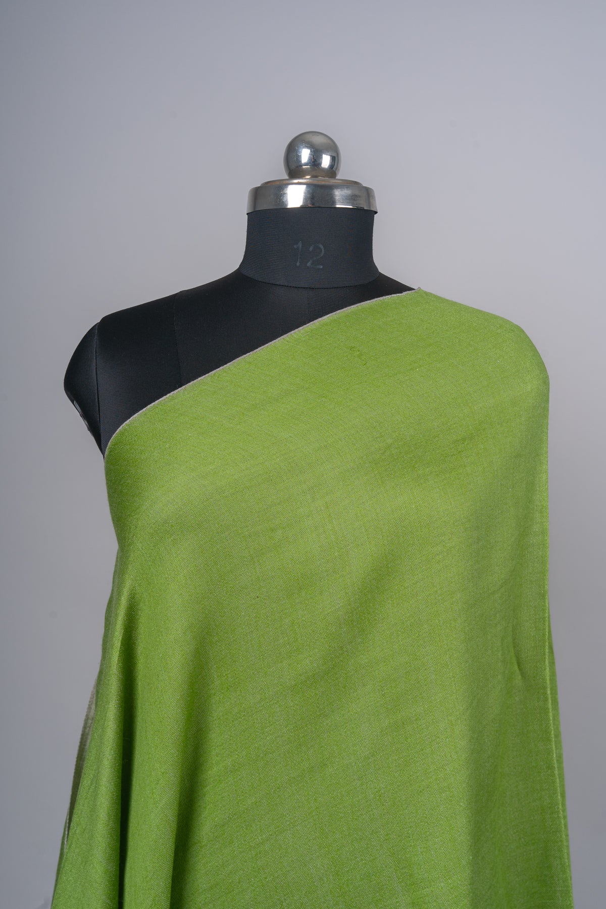 Close-up of a plain green stole over one shoulder of a black mannequin, showing its fine woven texture