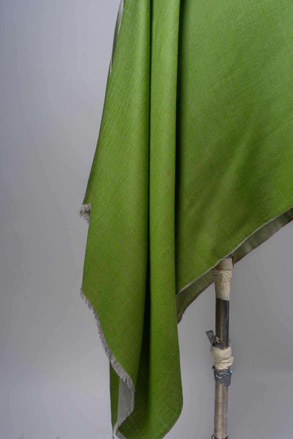 Close-up of the hanging folds and short fringed edge of a green Merino wool stole with a grey reverse
