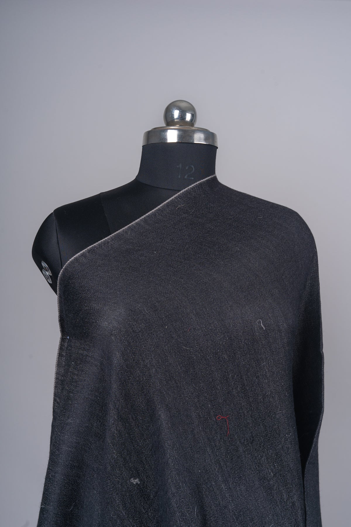 Close-up of the charcoal stole across a mannequin’s shoulder, showing its woven texture and thin grey edge