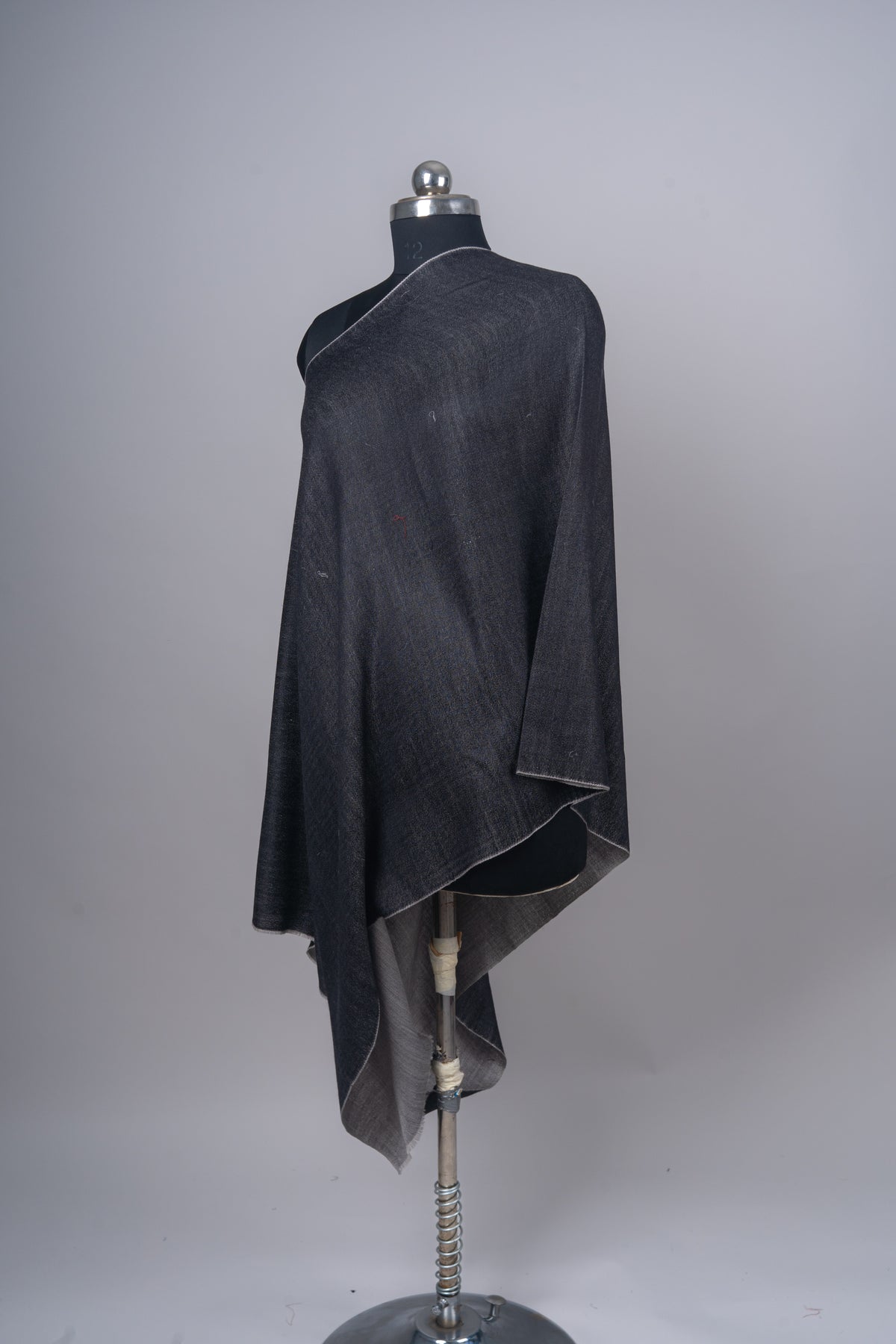 Angled full view of the charcoal stole draped over a mannequin, showing the contrasting grey underside at the hem