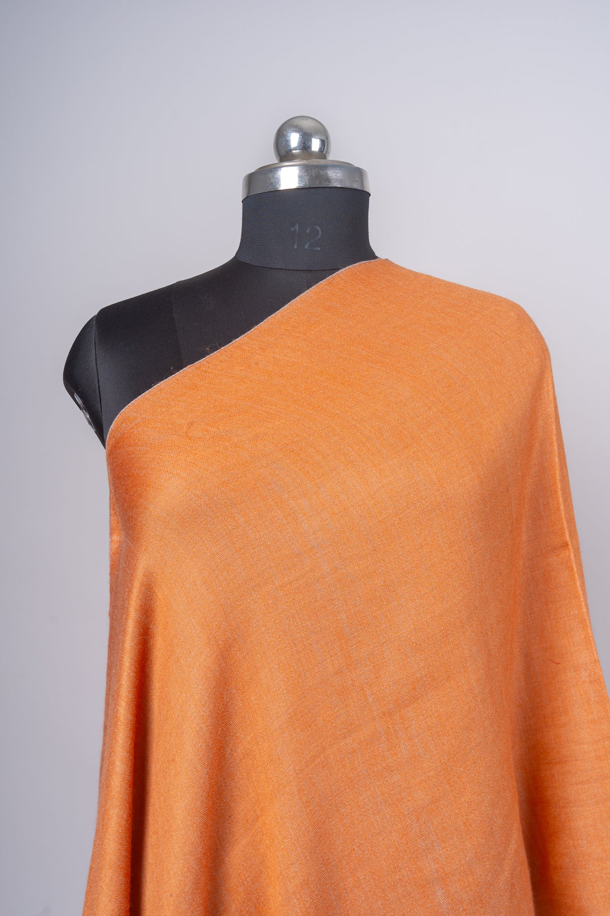 Close-up of plain amber Merino wool draped over one shoulder of a black mannequin, showing its fine weave