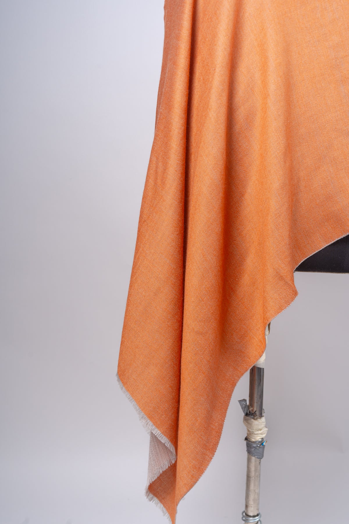 Detail of amber stole folds falling to a pointed corner, with a short fringe and beige reverse at the edge