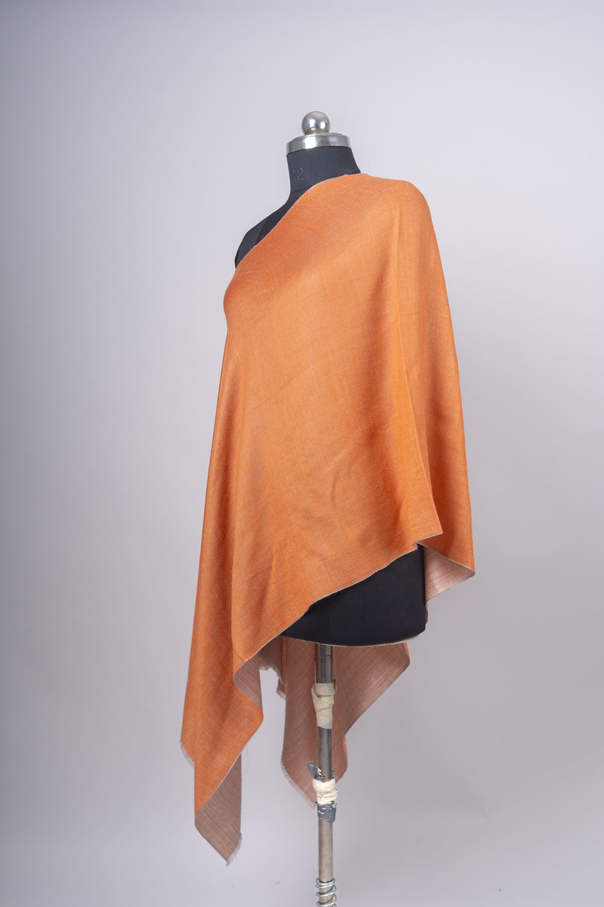 Side-angled amber stole on a mannequin with the beige reverse turned outward beneath the draped edge