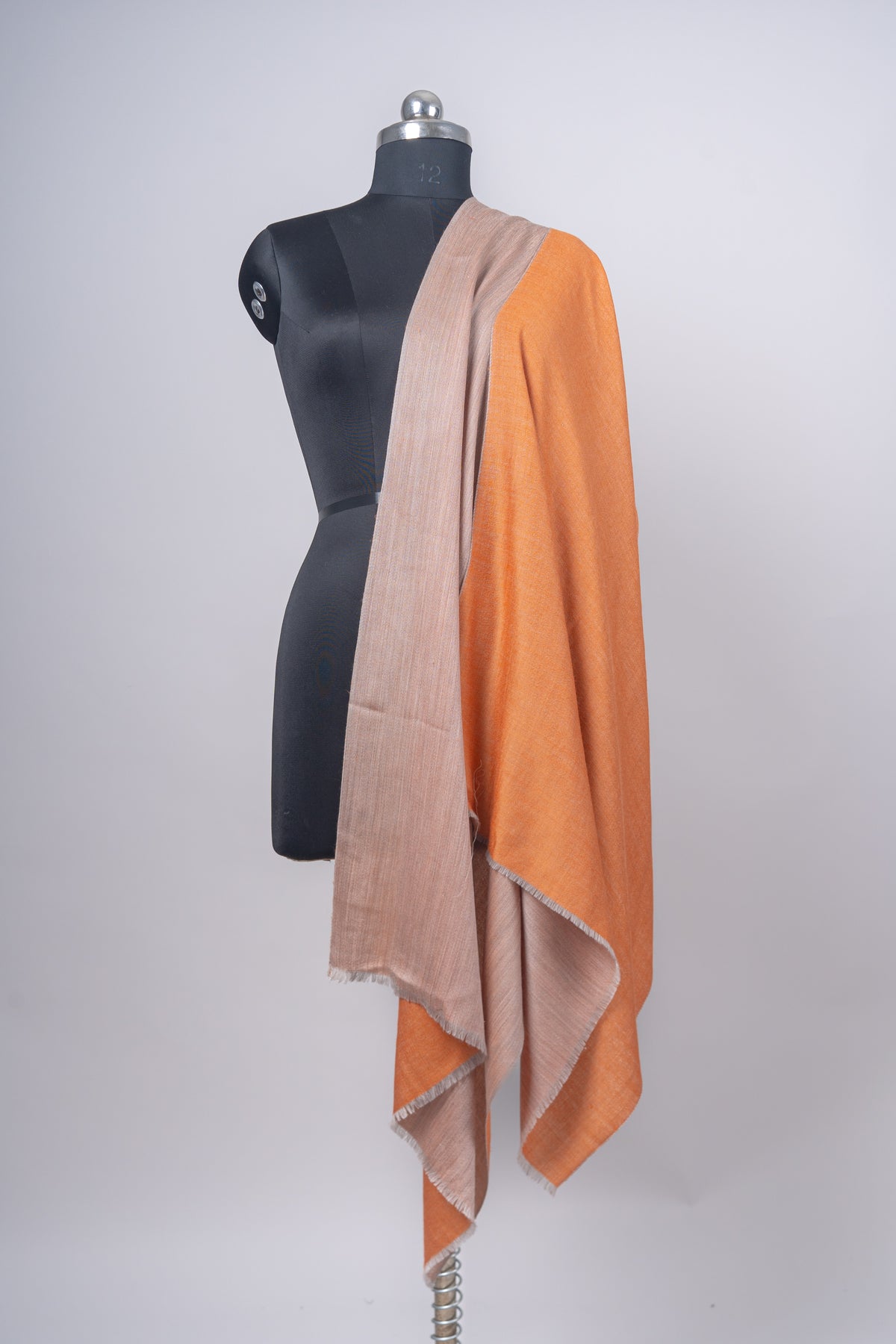 Reversible stole hanging over one shoulder of a mannequin, showing long amber and sandstone-beige panels side by side