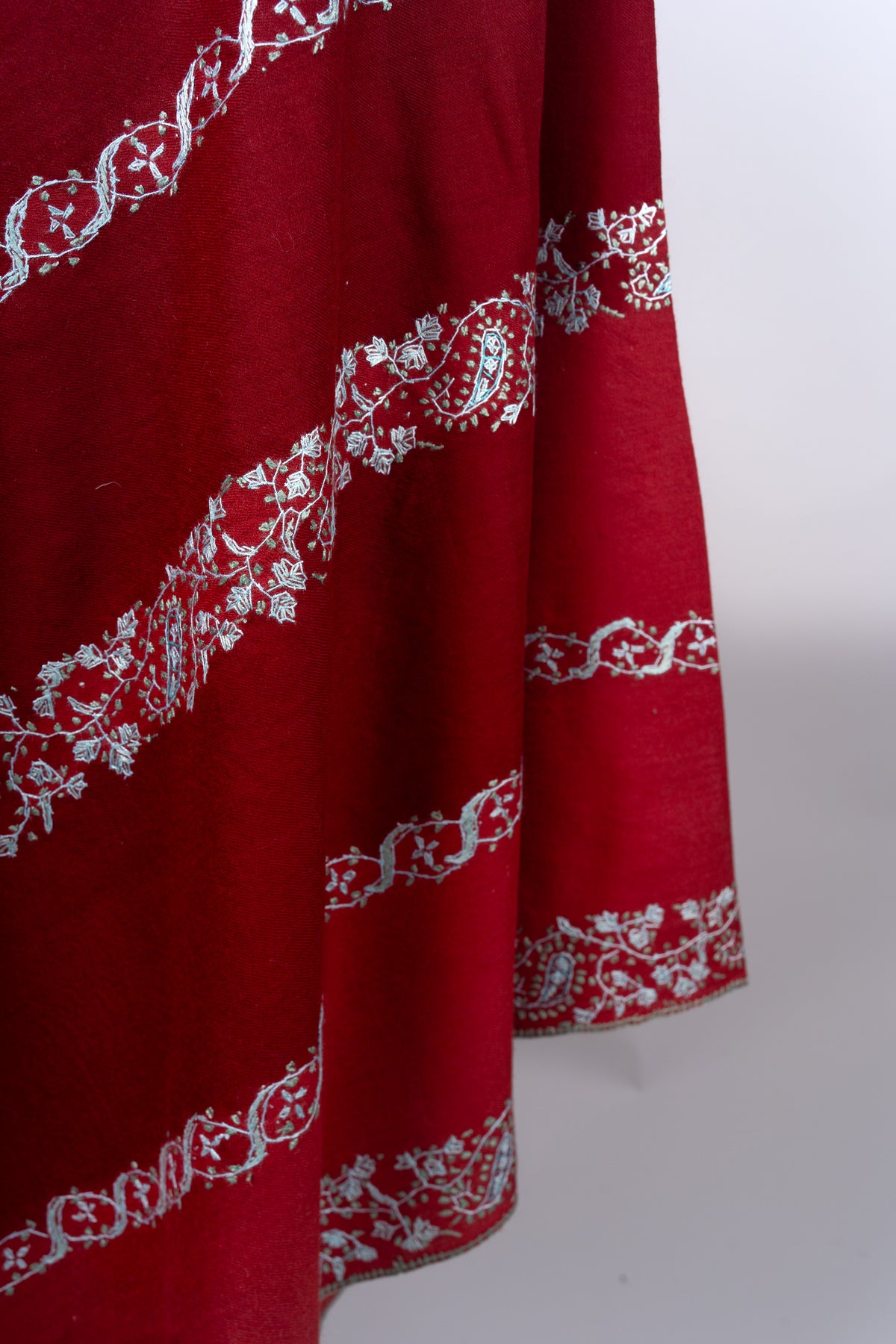 Detail of pale blue paisley, flower and looping vine embroidery across the crimson shawl’s hanging folds