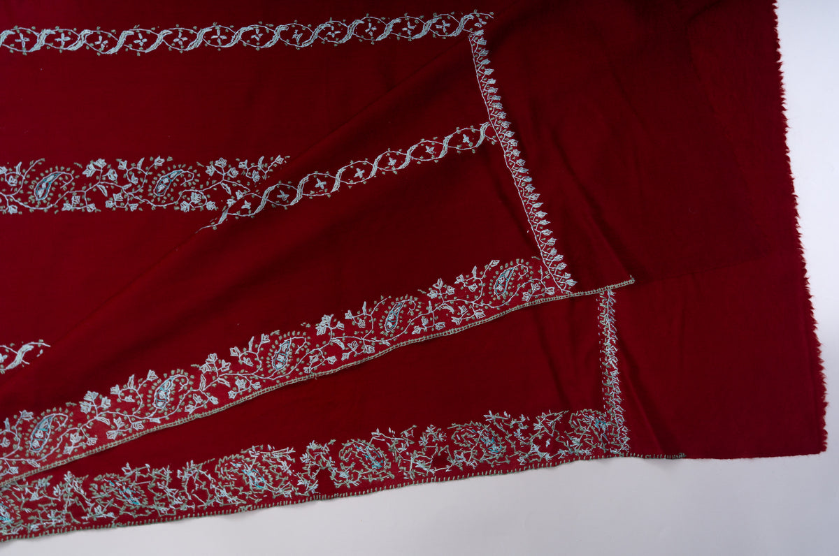Folded corner of the crimson Sozni shawl showing pale blue floral borders, narrow edge embroidery and a plain fringed end