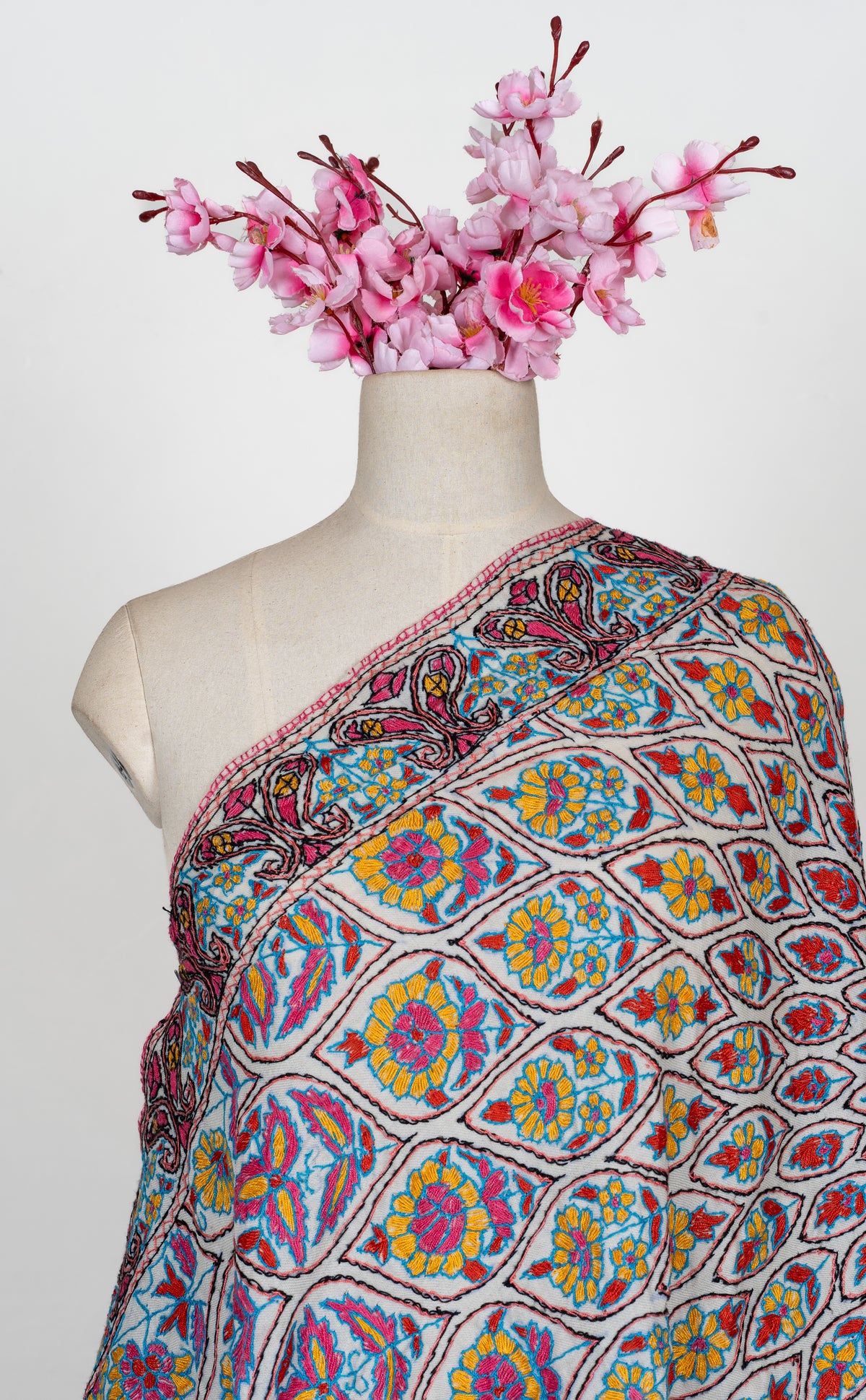 Ivory Merino wool stole draped across a mannequin with blue, yellow and pink Sozni flowers inside a dark-outlined lattice