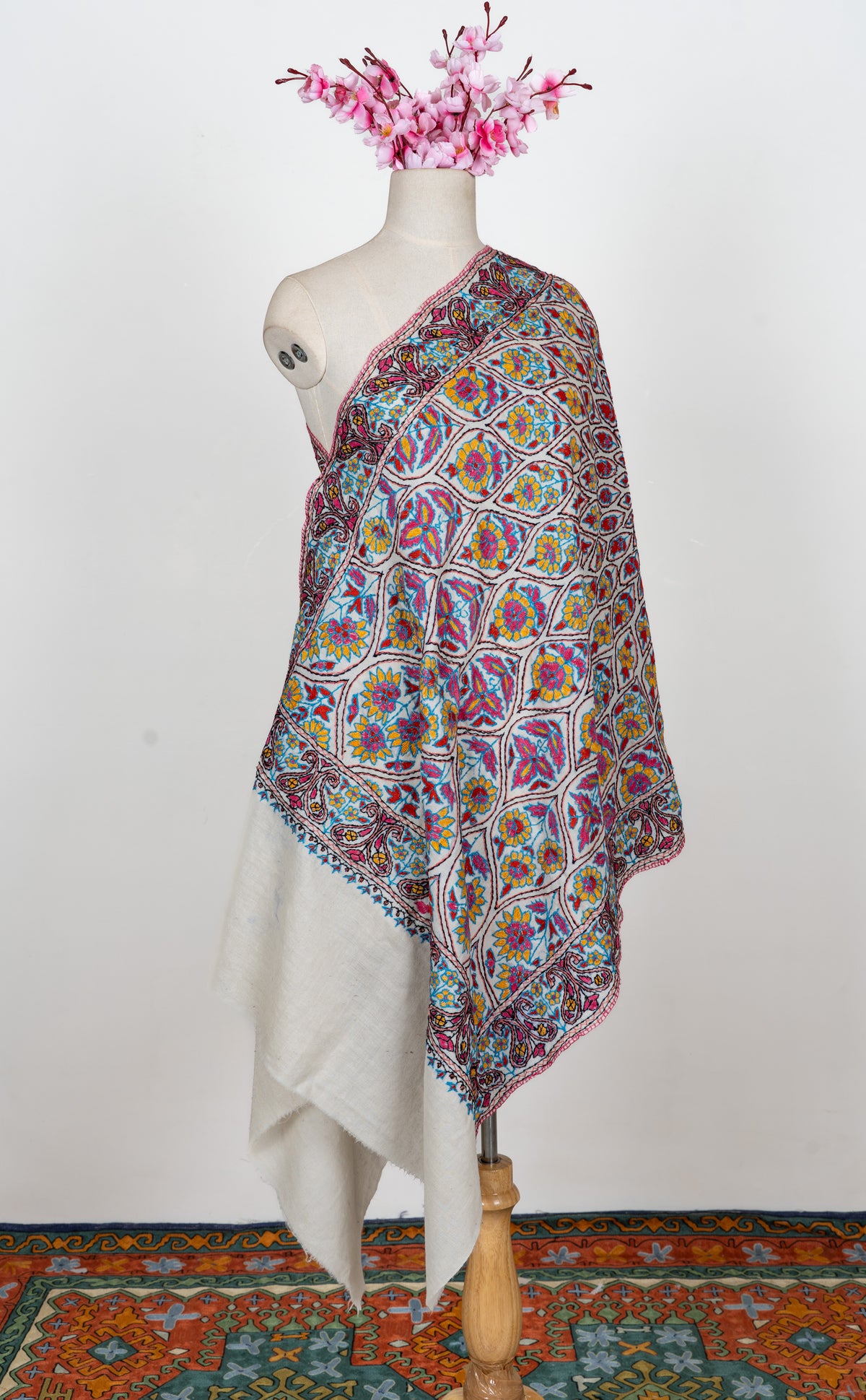 Full-length ivory stole on a mannequin with blue, yellow and pink Sozni floral medallions and patterned borders
