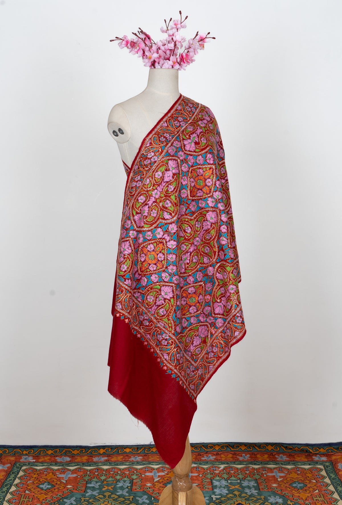 Full-length view of a red Merino wool stole on a mannequin with multicoloured Sozni floral panels and a plain red end.