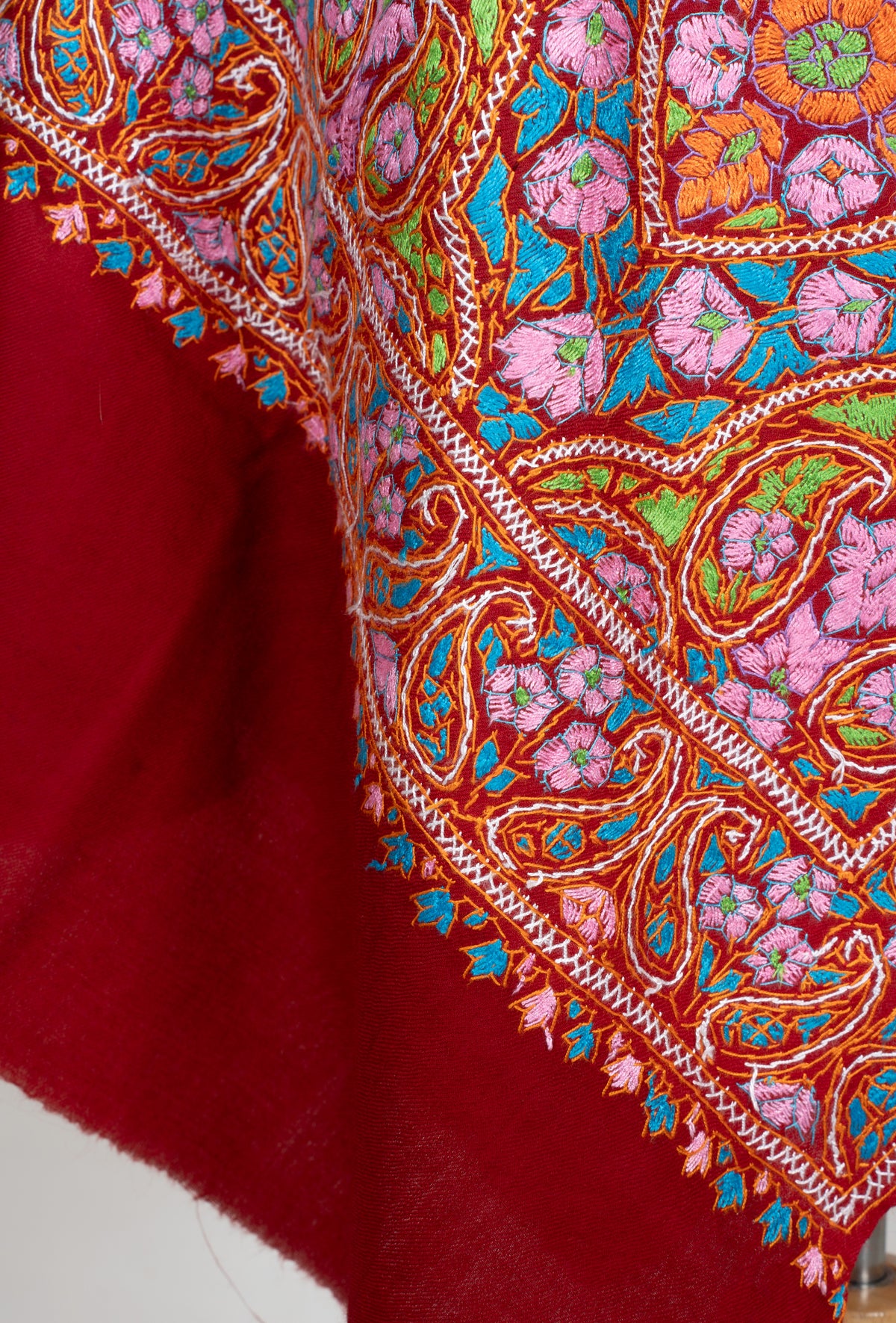 Draped end of a red Merino wool stole with colourful Sozni flowers, a paisley border and small leaf edging.