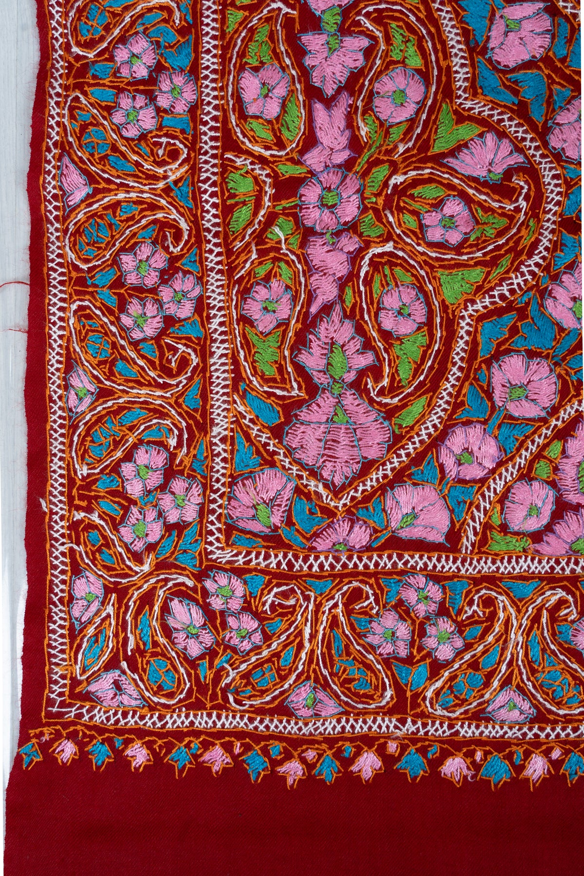 Corner detail of a red Merino wool stole with pink Sozni flowers, green paisleys, turquoise leaves and a paisley border.