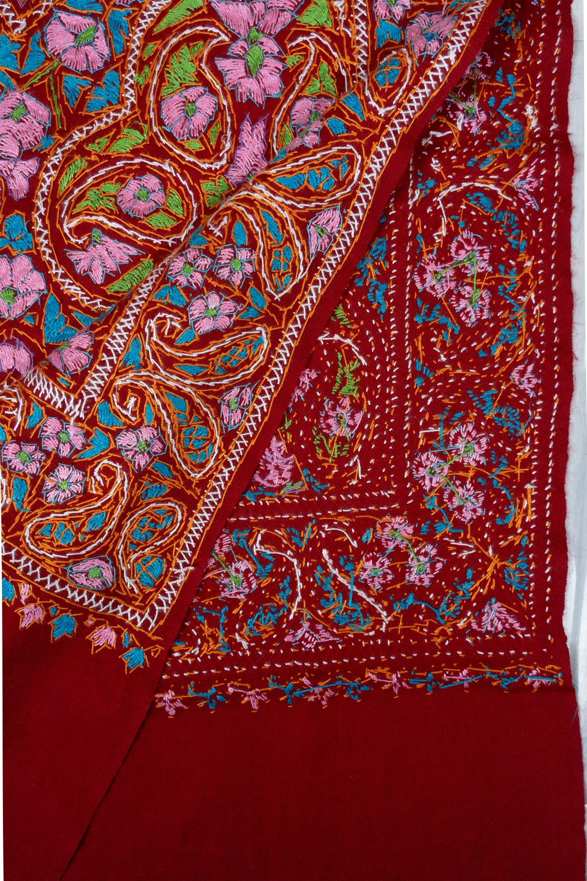 Folded corner showing the front and reverse of dense multicoloured Sozni floral stitching on a red Merino wool stole.