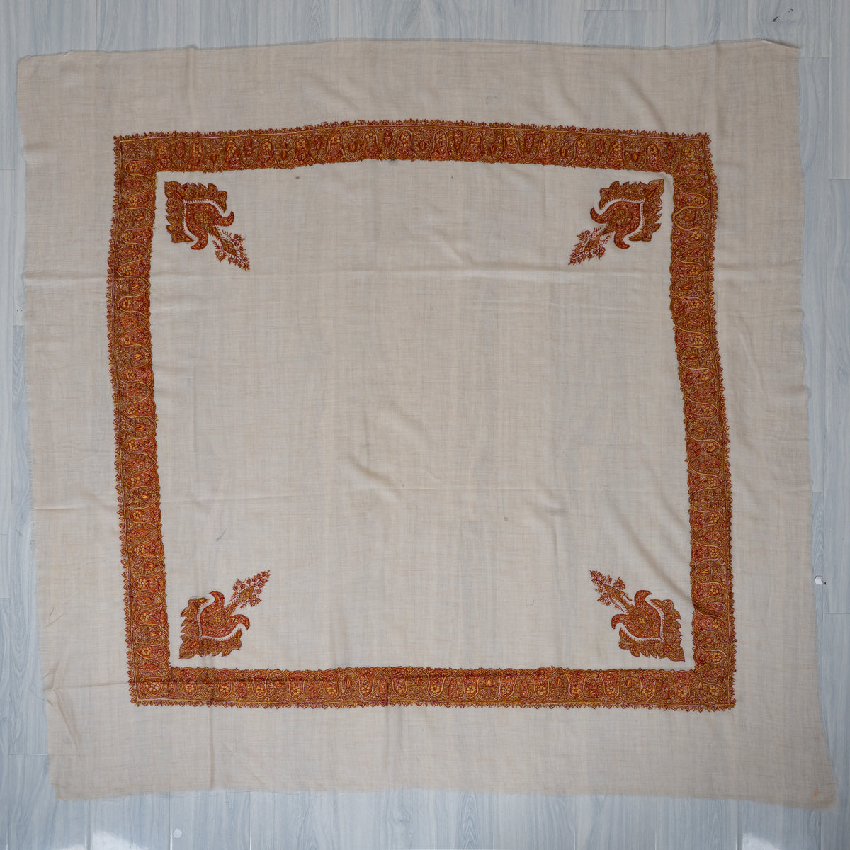 Ivory square rumal laid flat, with a saffron and maroon embroidered border and four ornate floral corner motifs