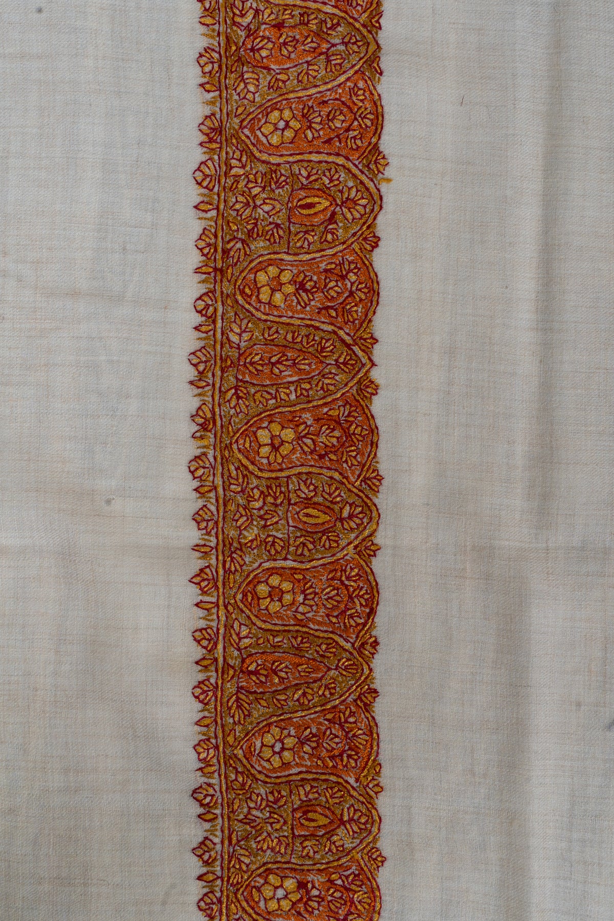Close-up of a rumal border with saffron and maroon paisleys filled with small flowers and leafy edging on ivory fabric