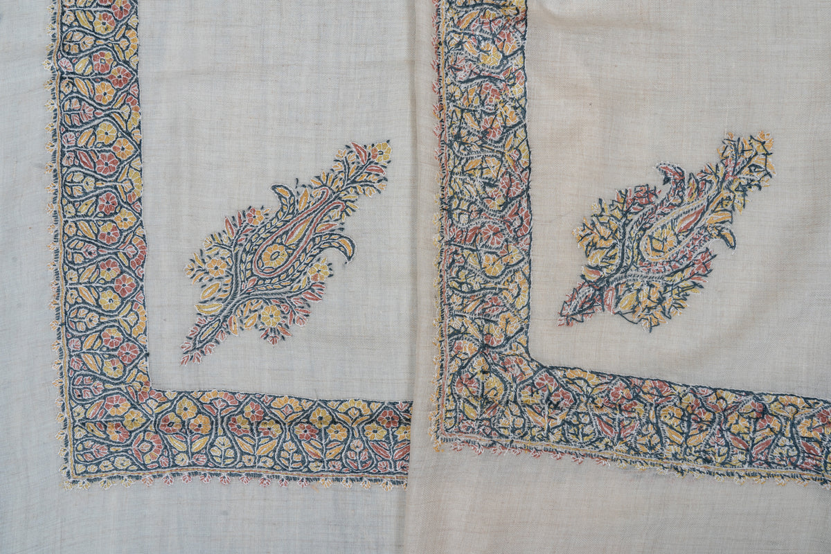Overlapping ivory rumal corners showing the front and reverse of pastel floral embroidery