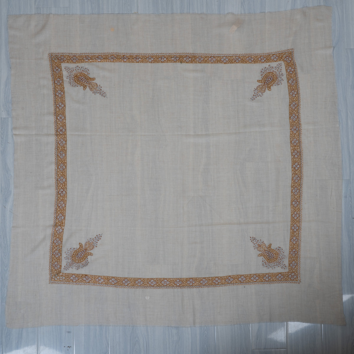Cream square cashmere rumal laid flat, with a honey-gold embroidered border and four pale blue and gold corner motifs