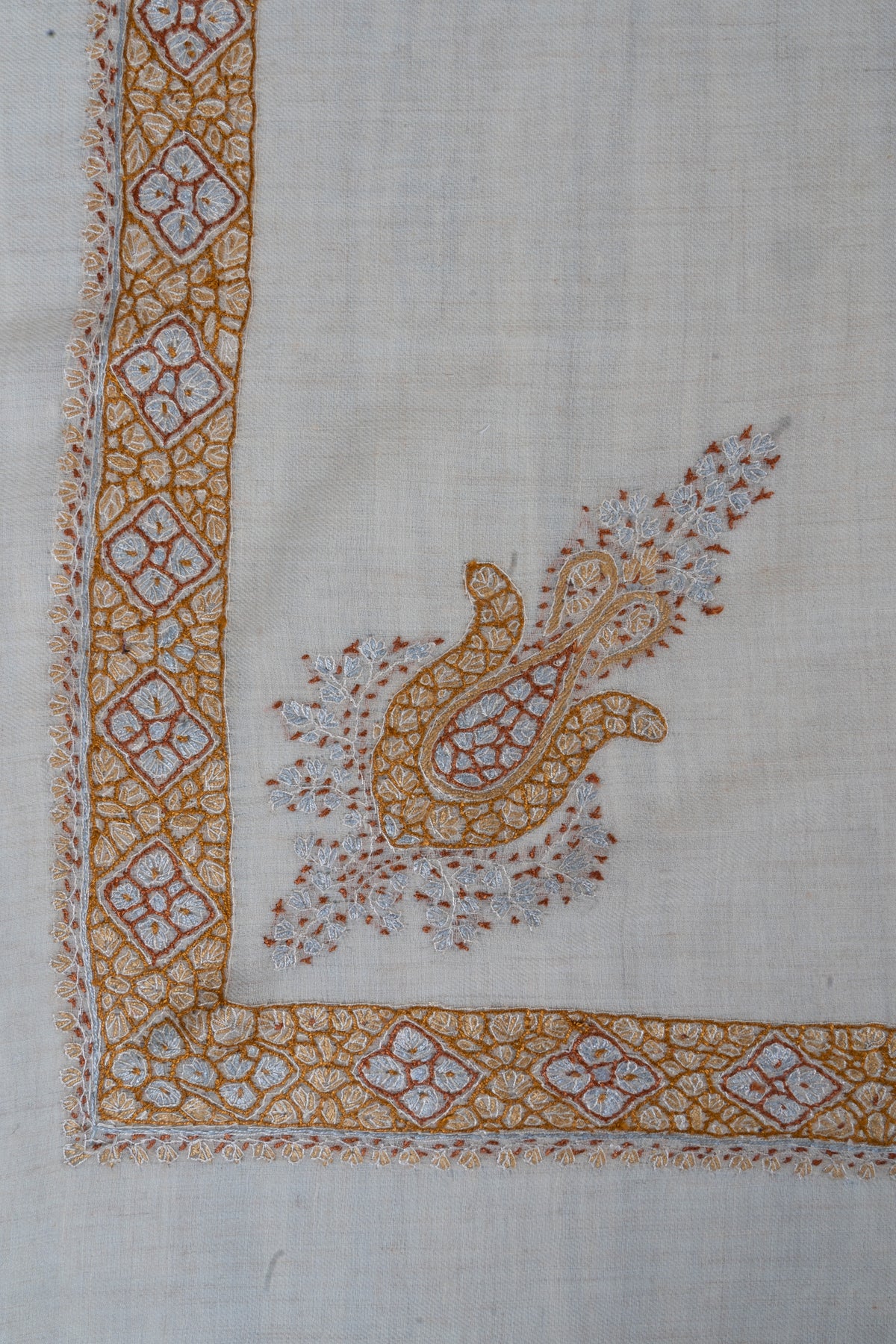 Cream rumal corner with a honey-gold and pale blue Sozni floral motif beside a narrow geometric border