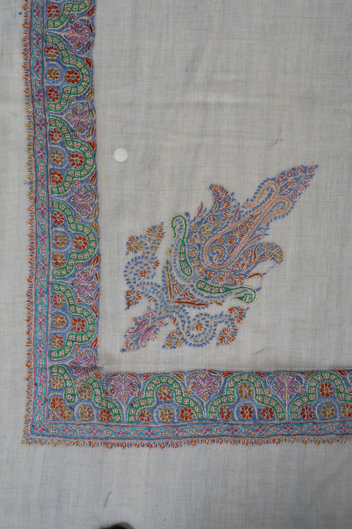 Corner of a cream cashmere rumal with a blue, green and pink Sozni paisley and a matching floral border.