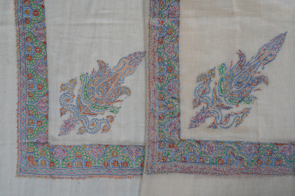 Two cream cashmere rumal corners showing multicoloured paisleys and the front and reverse of Sozni floral border stitching.