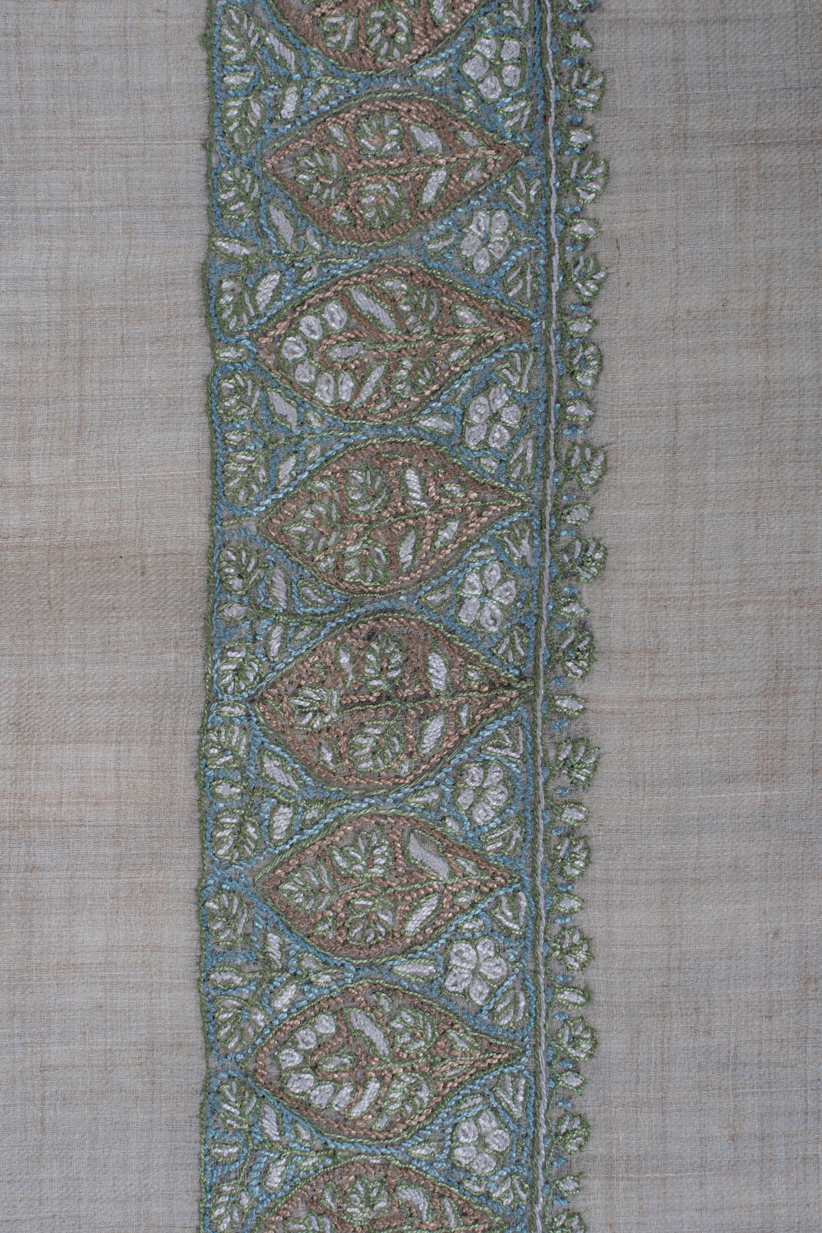 Close-up of the sage and aqua embroidered border with repeating leaf-shaped floral medallions