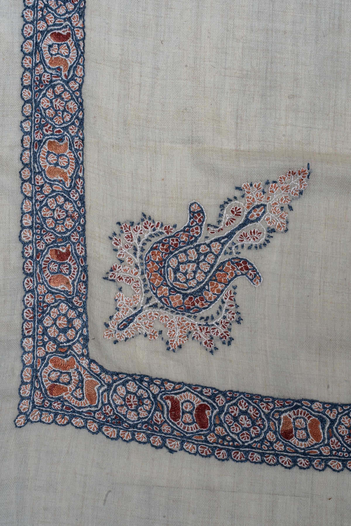 Ivory rumal corner with an indigo and rust Sozni floral motif beside a border of alternating floral medallions