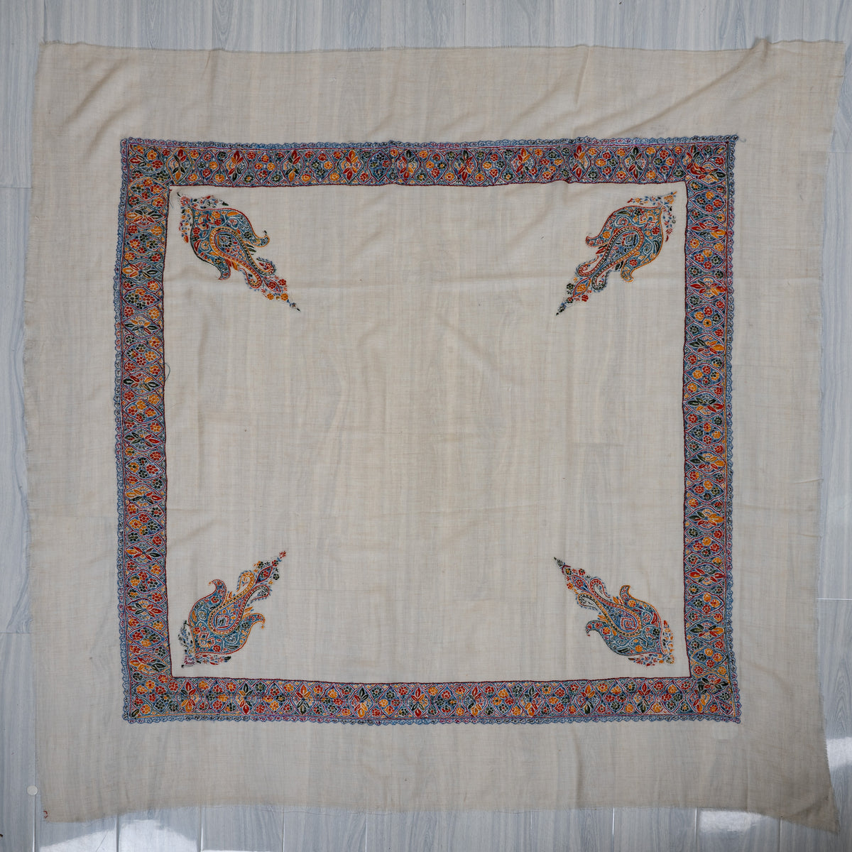 Cream cashmere rumal laid flat, with a square multicoloured floral border and four paisley corner motifs