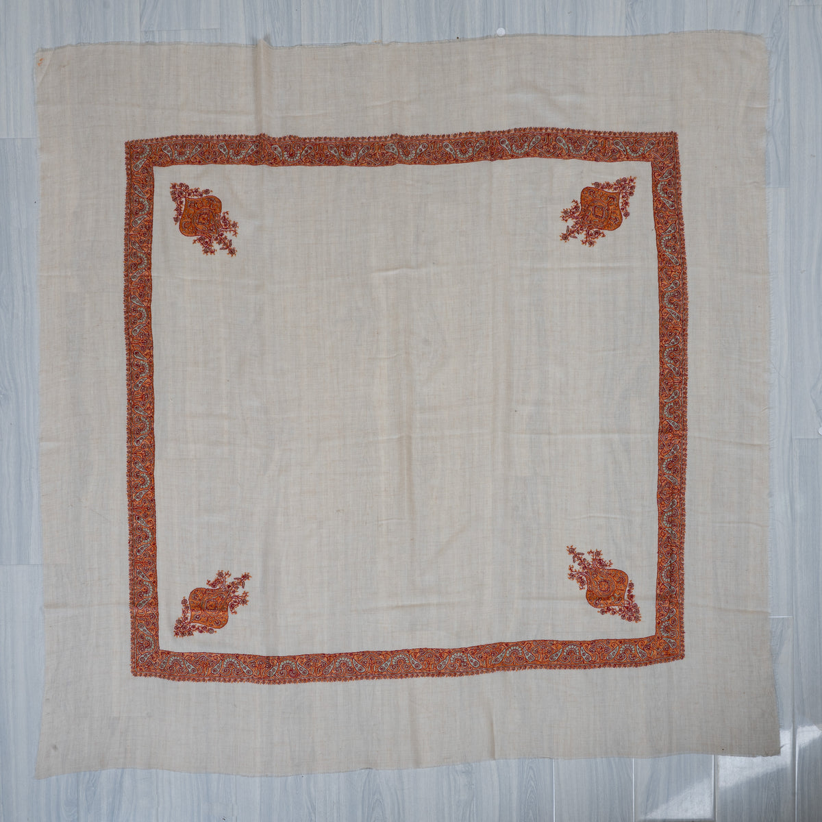 Ivory square cashmere rumal laid flat, with a burnt-orange patterned border and four ornate floral corner motifs